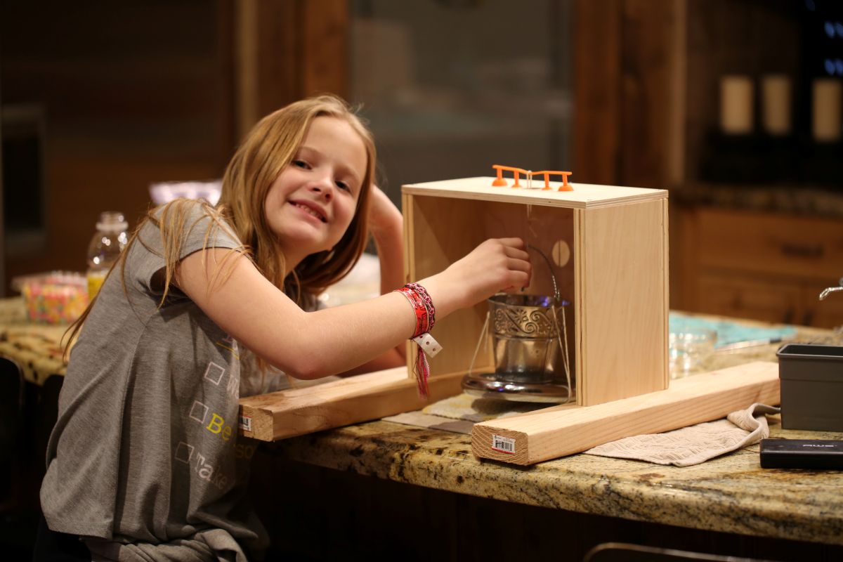 Amber Parker with her 5th grade science fair project. She hung weights off a 3D-printed bridge to test its strength. In addition to a five-pound weight, she is dropping washers into the metal bucket to add more weight. Photo courtesy of MeriAnn Freestone-Parker.