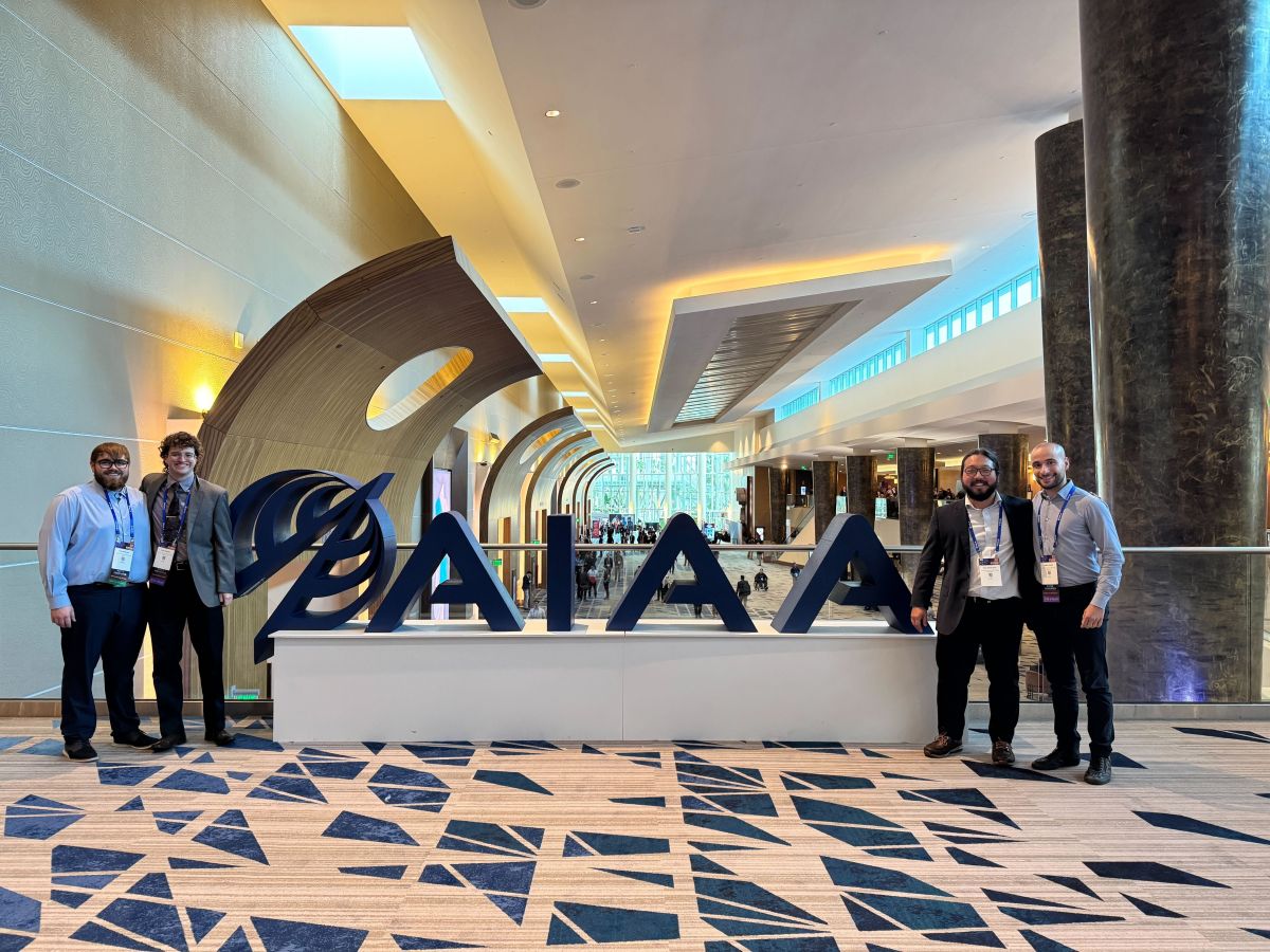 Aerospace grad students left to right: Tyler Gralewski, Marty Bathgate, Elias Waddington and Matteo Guidotti pose with the giant AIAA sign at the 2026 Scitech Forum in Orlando.