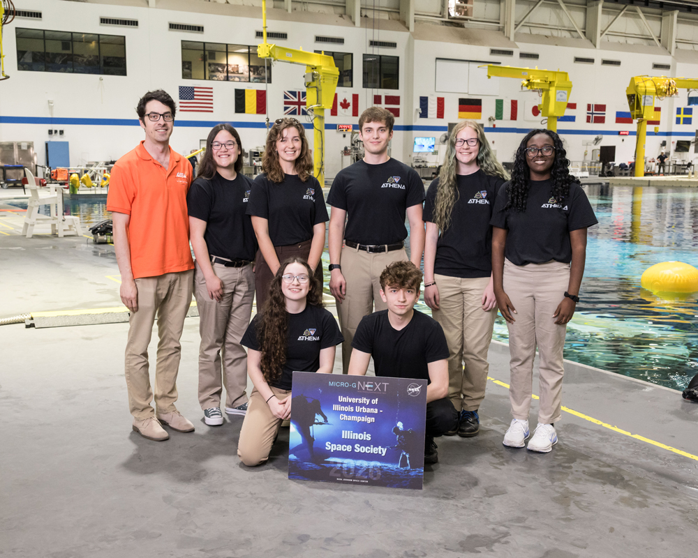 The U of I Micro-g NExT test week team in front of the Neutral Bouyancy Laboratory pool. From left to right: Mickey Clemon, Katelyn Czarnowski, Lillian Hunt, Casimir Pawlowski, Isabel Obert, Tiana Foreman, Alana Falter, Max Alchin.
