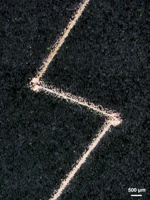 The coating, applied to a steel plate, brightly highlights a thin zigzag scratch.