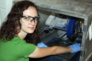 Yolanda Dionicio, an Aerospace Engineering undergraduate, uses a saw to cut varying lengths of specimens that contain sacrificial fibers embedded in epoxy resin system. After cutting the desired specimens, Dionicio will place them in the oven for a full evacuation study. The sacrificial fiber will degrade leaving behind empty channels to incorporate a microvascular network into a matrix material.