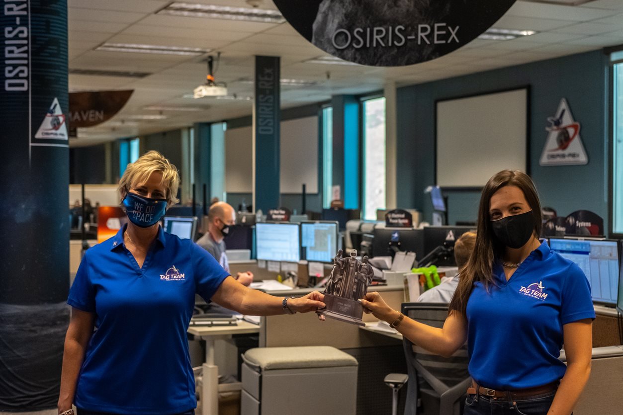 Holding a flat Alma at OSIRIS-Rex mission operations, Coralie Adam, BS &acirc;&euro;&trade;11, with fellow AE alumni, Beth Buck, BS &acirc;&euro;&tilde;89, who oversaw the deep space mission operations at Lockheed Martin, including OSIRIS-Rex